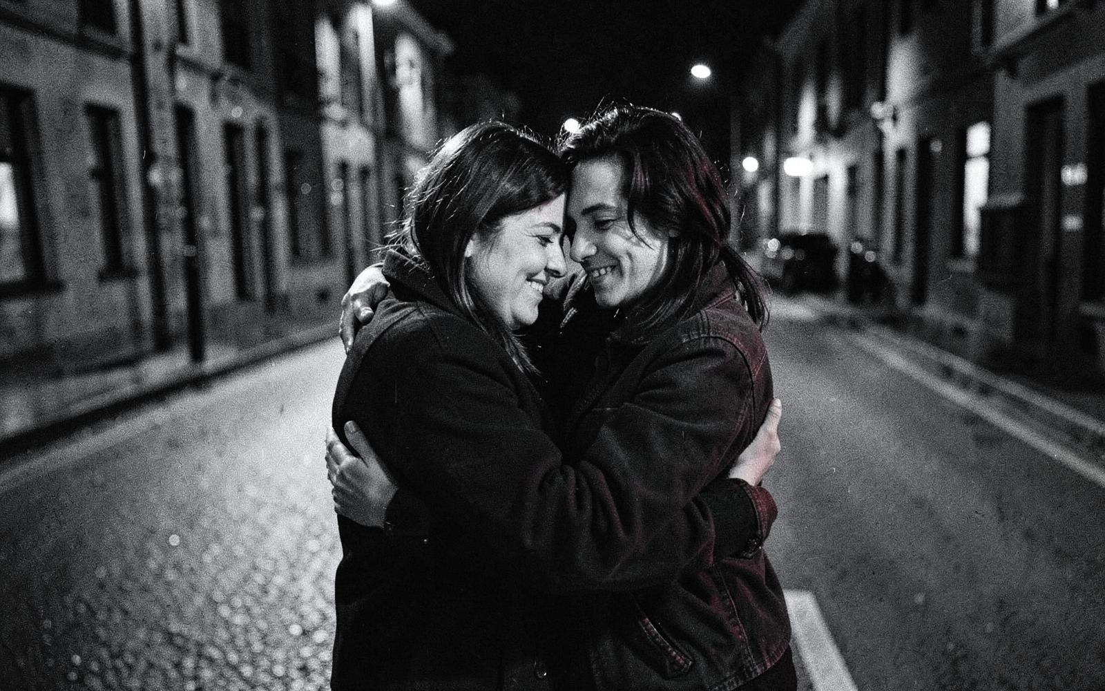 Two friends holding onto each other on a quiet street at night